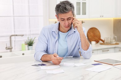 Photo of Paying bills. Man with different invoices talking on phone at table indoors