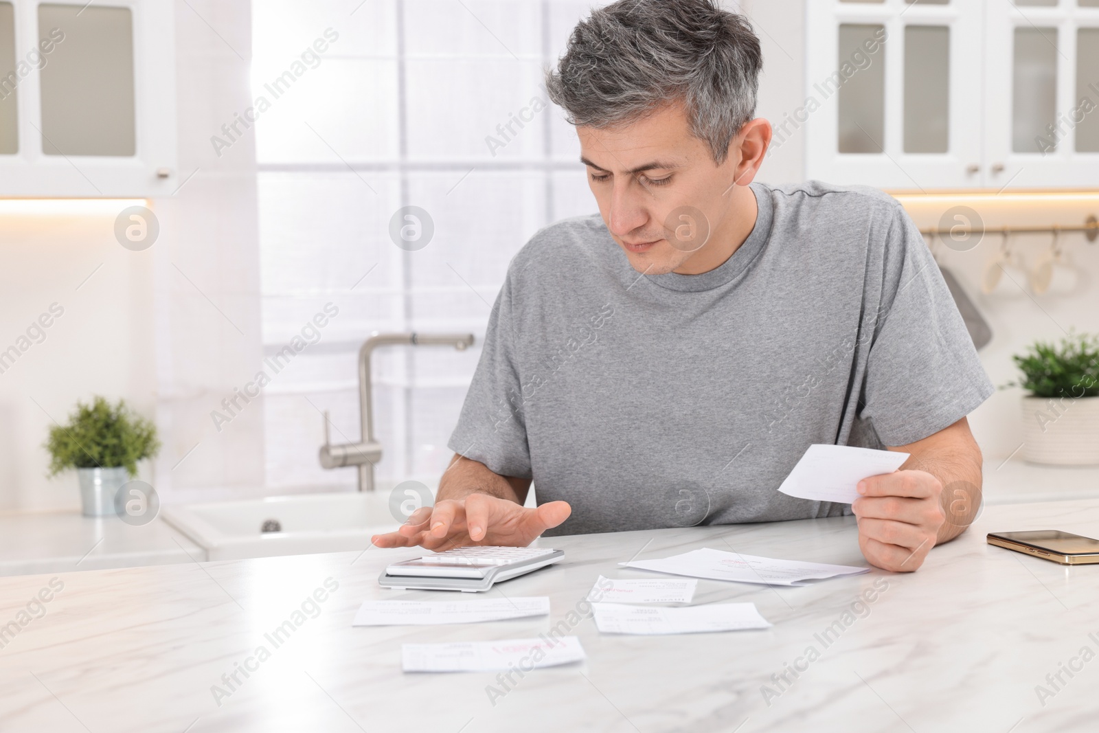 Photo of Paying bills. Man with different invoices using calculator at white marble table indoors