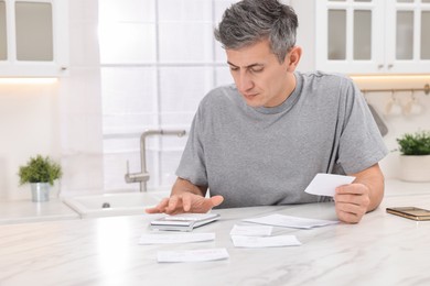 Photo of Paying bills. Man with different invoices using calculator at white marble table indoors