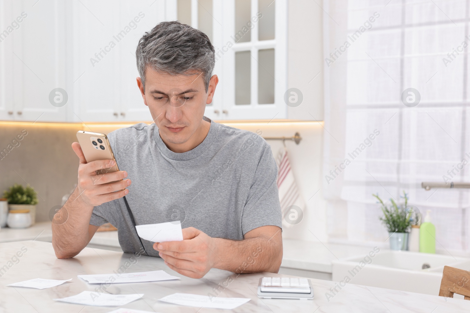 Photo of Man paying bills with smartphone at white marble table indoors