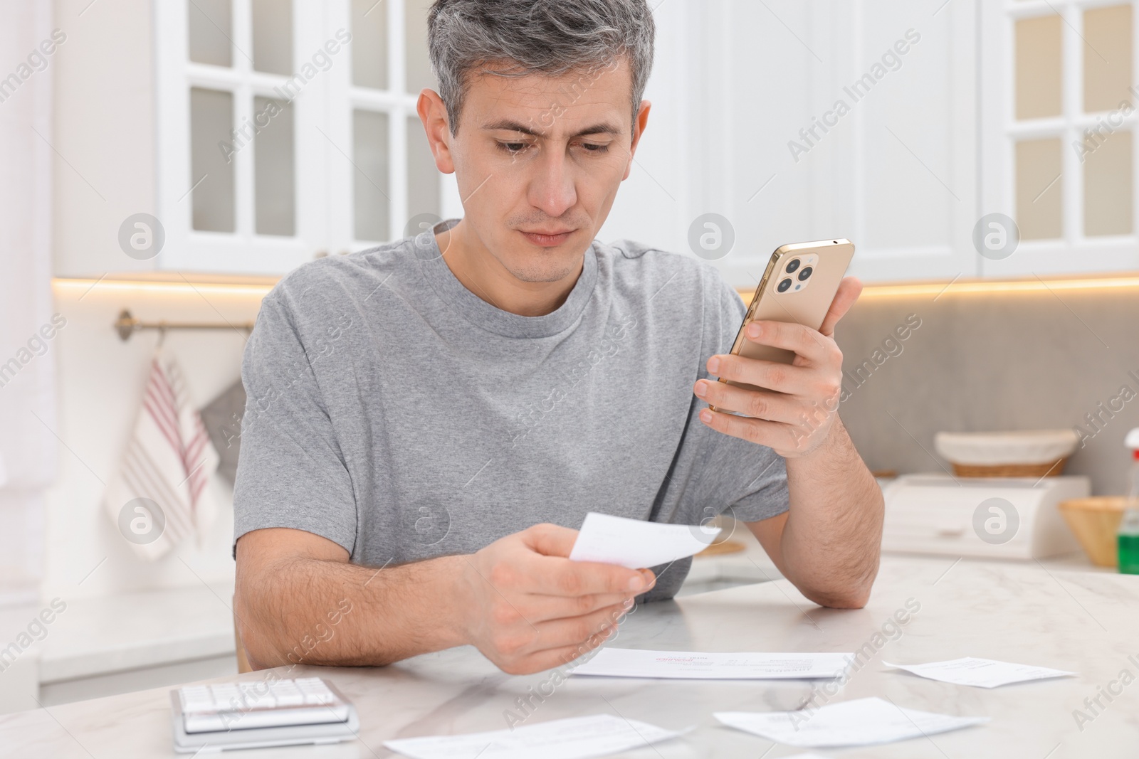 Photo of Man paying bills with smartphone at white marble table indoors