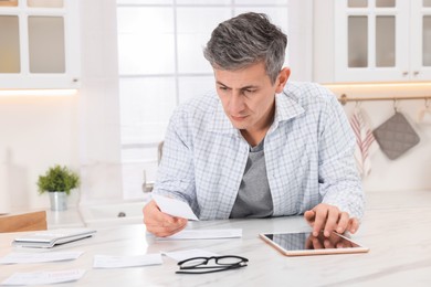 Photo of Man paying bills with tablet at white marble table indoors