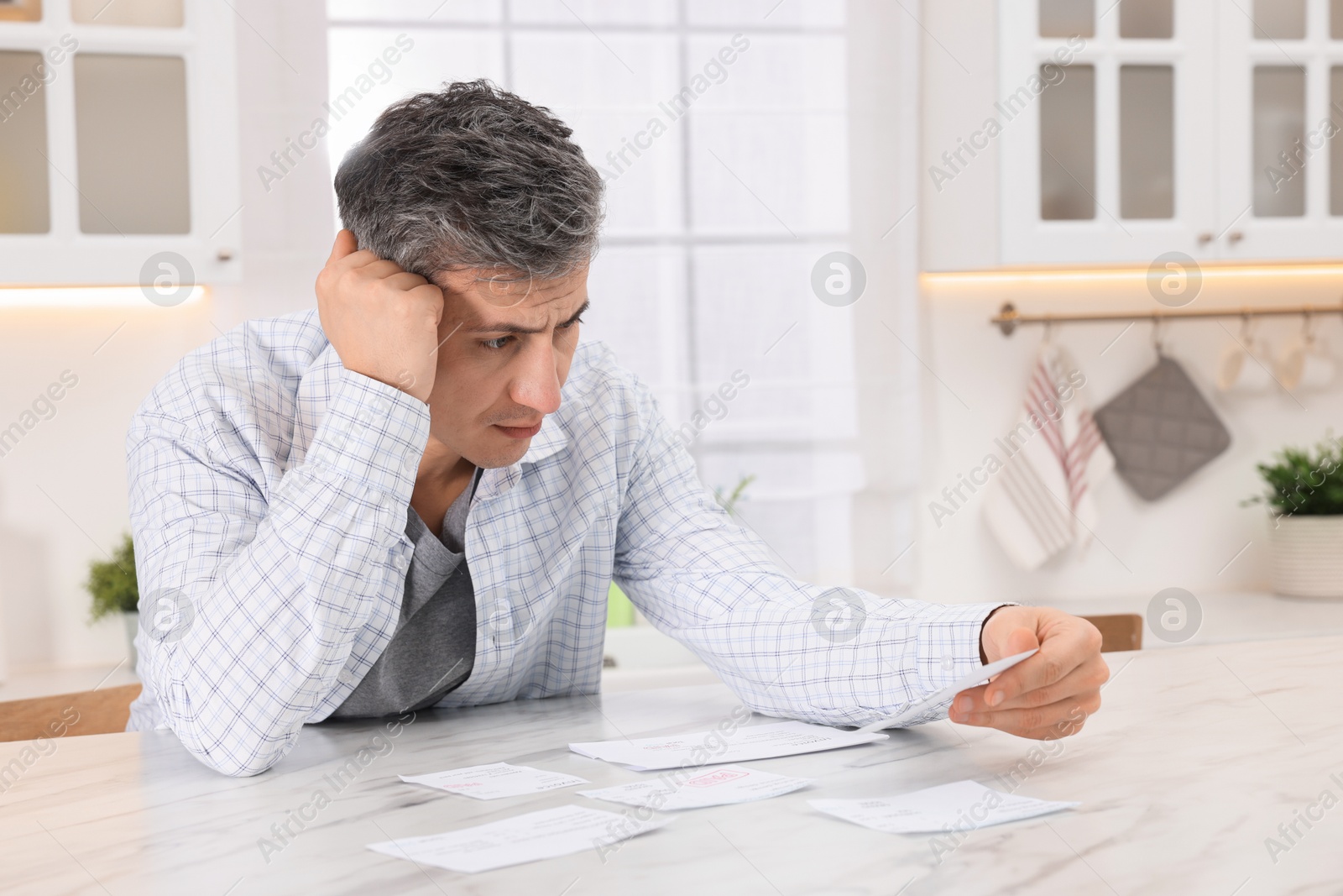 Photo of Paying bills. Confused man with different invoices at white marble table indoors