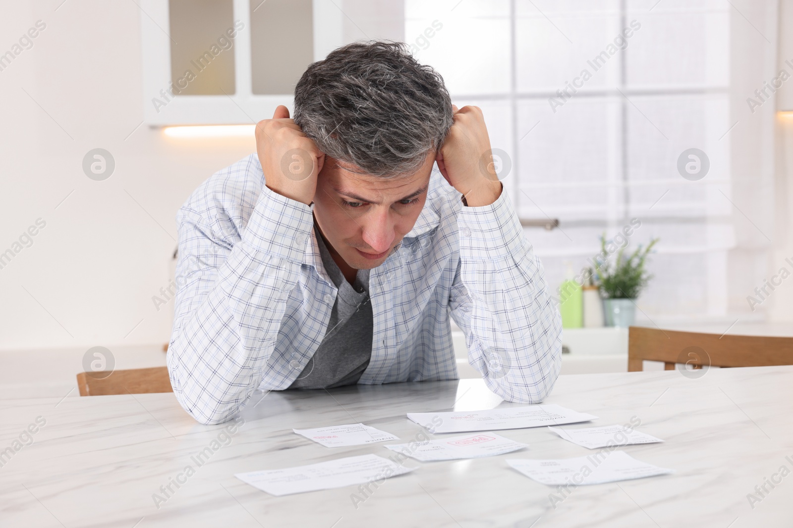 Photo of Paying bills. Confused man with different invoices at white marble table indoors