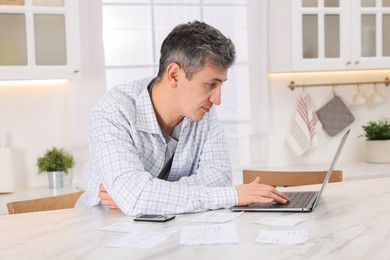 Photo of Man paying bills with laptop at white marble table indoors