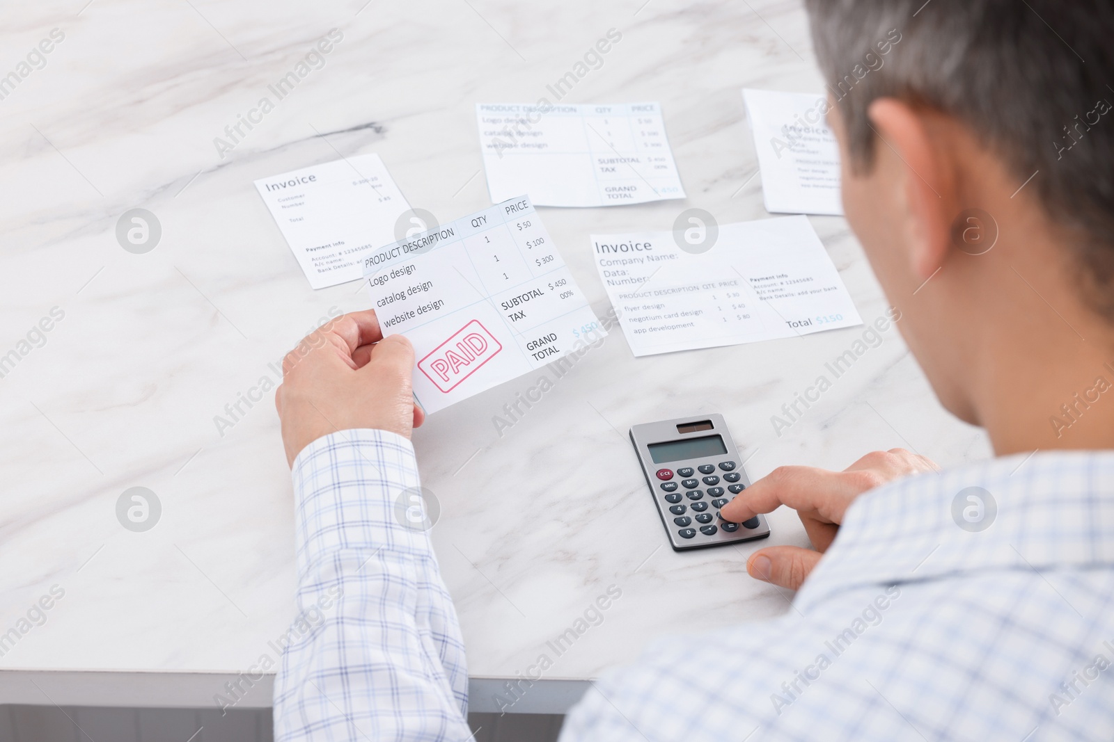 Photo of Paying bills. Man with different invoices using calculator at white marble table, above view