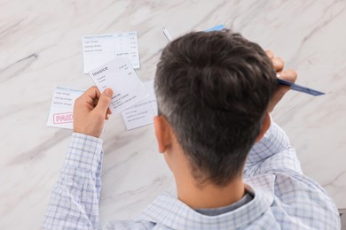 Photo of Paying bills. Man with different invoices at white marble table, above view