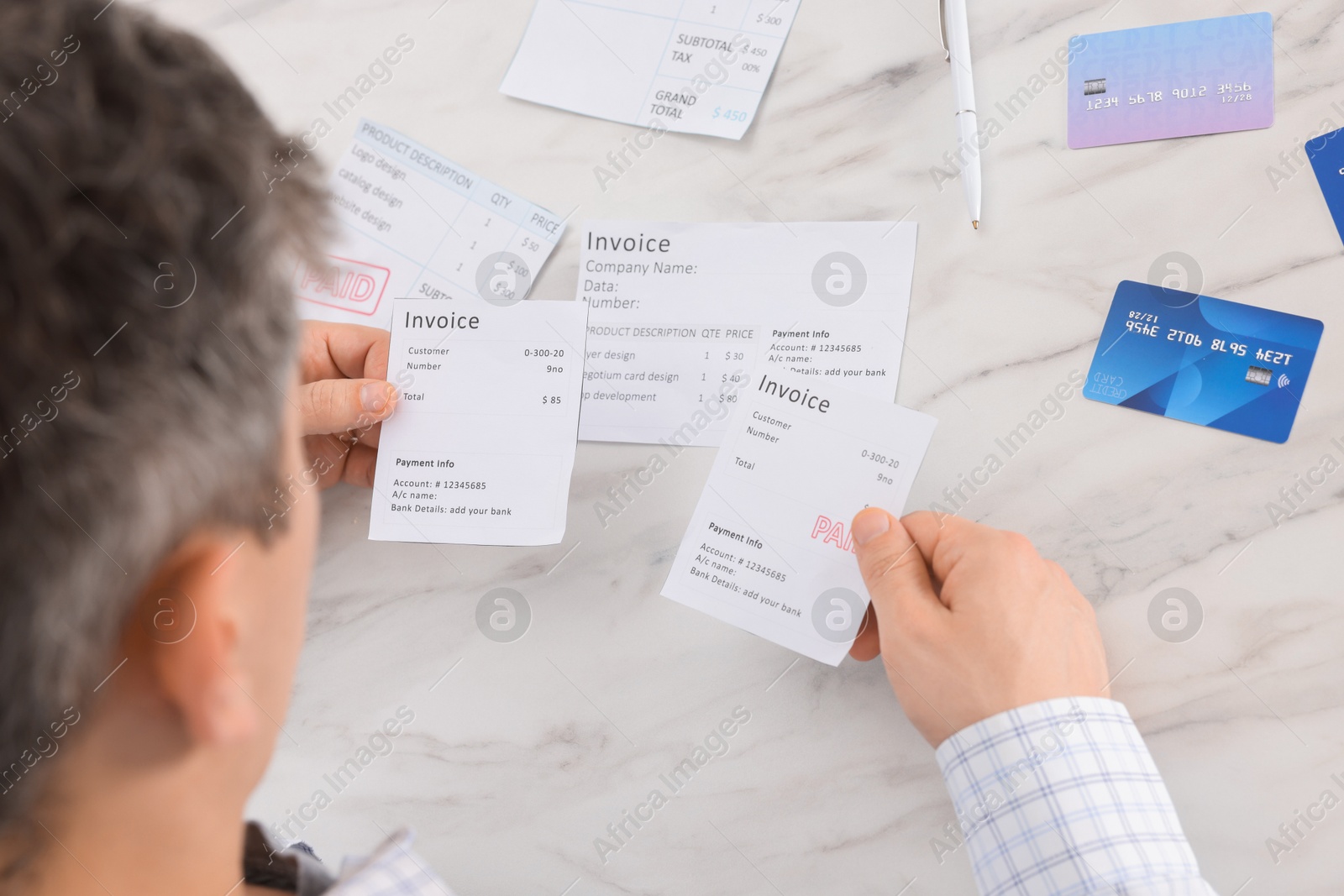 Photo of Paying bills. Man with different invoices and credit cards at white marble table, closeup