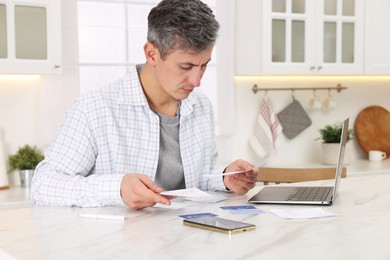 Photo of Paying bills. Man with reviewing invoices at white marble table indoors