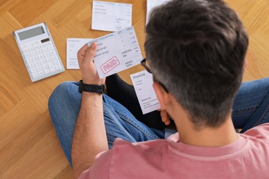 Photo of Paying bills. Man with different invoices using calculator on floor indoors, above view