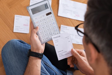 Photo of Paying bills. Man with different invoices using calculator on floor indoors, closeup