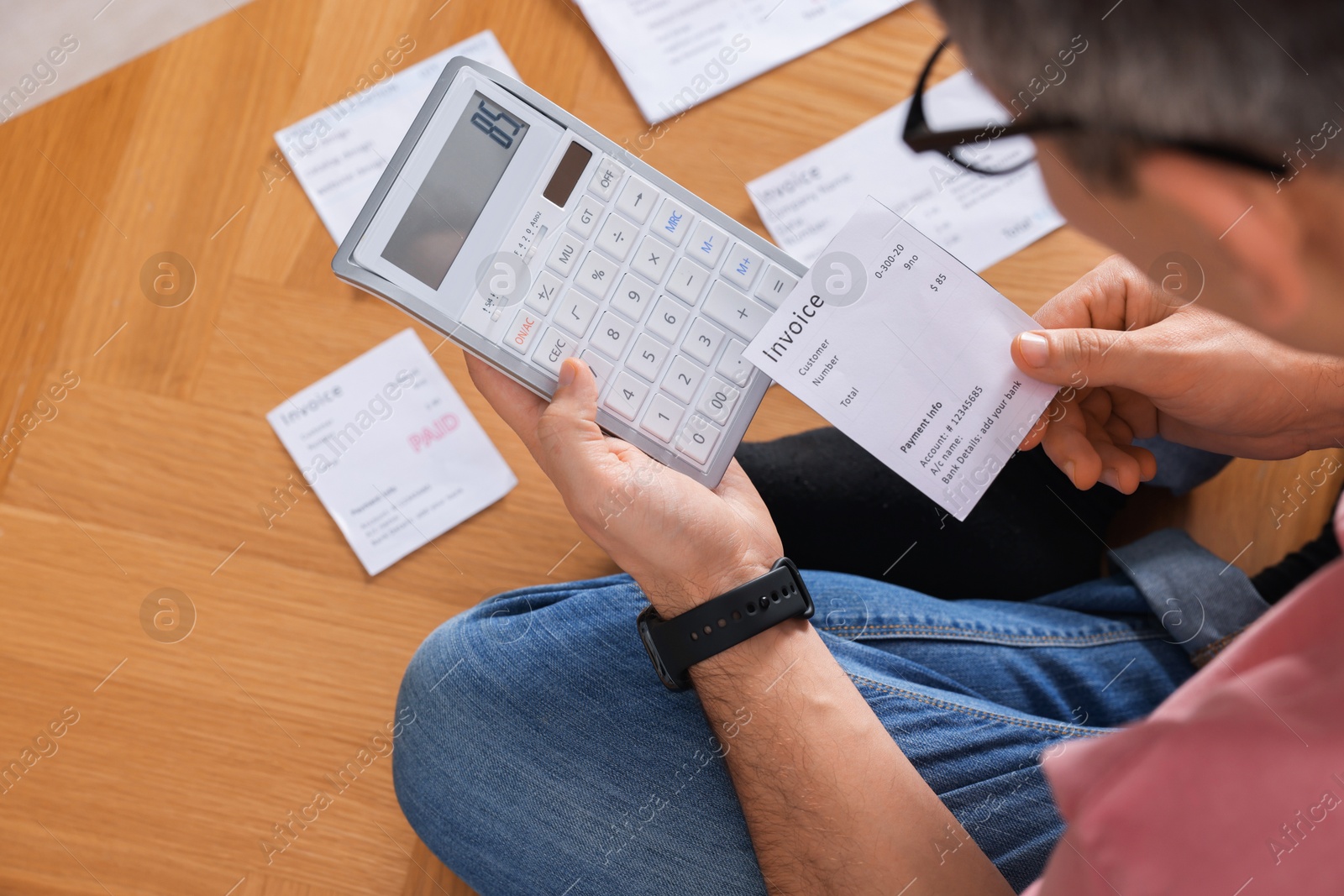 Photo of Paying bills. Man with different invoices using calculator on floor indoors, closeup