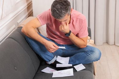 Photo of Paying bills. Man with different invoices on sofa indoors