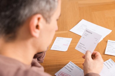 Photo of Paying bills. Man with different invoices at wooden table, closeup