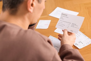 Photo of Paying bills. Man with different invoices at wooden table, closeup