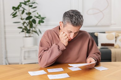 Photo of Paying bills. Man with different invoices at wooden table