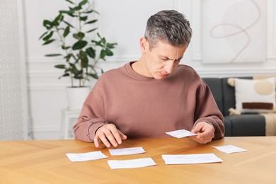 Photo of Paying bills. Man with different invoices at wooden table