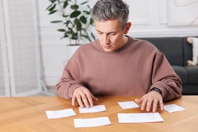 Photo of Paying bills. Man with different invoices at wooden table