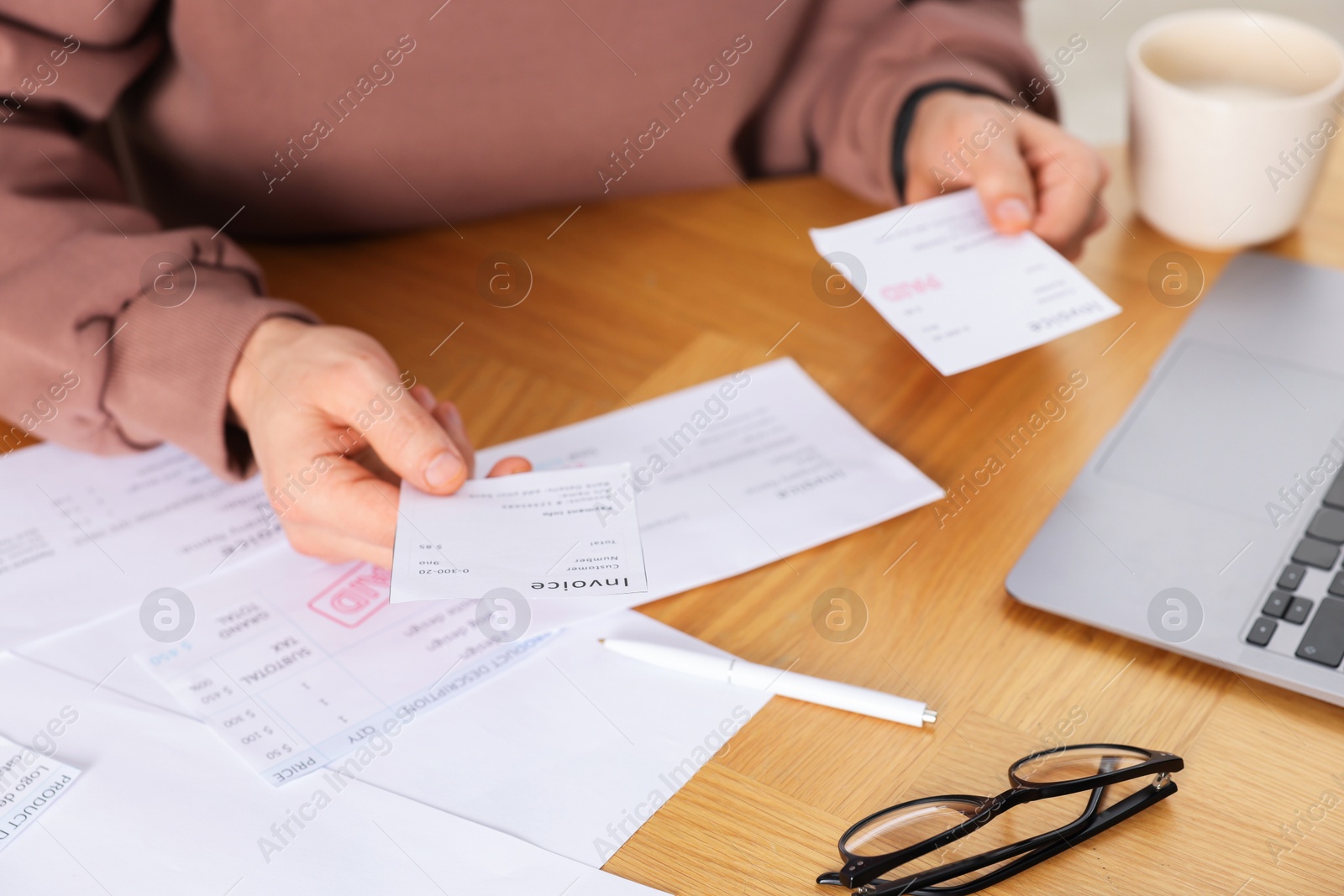 Photo of Paying bills. Man with reviewing invoices at wooden table indoors, closeup