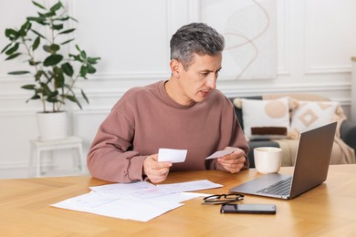 Photo of Man paying bills with laptop at wooden table indoors