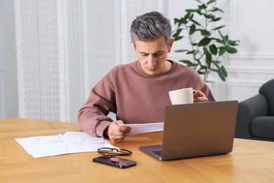 Photo of Man paying bills with laptop at wooden table indoors