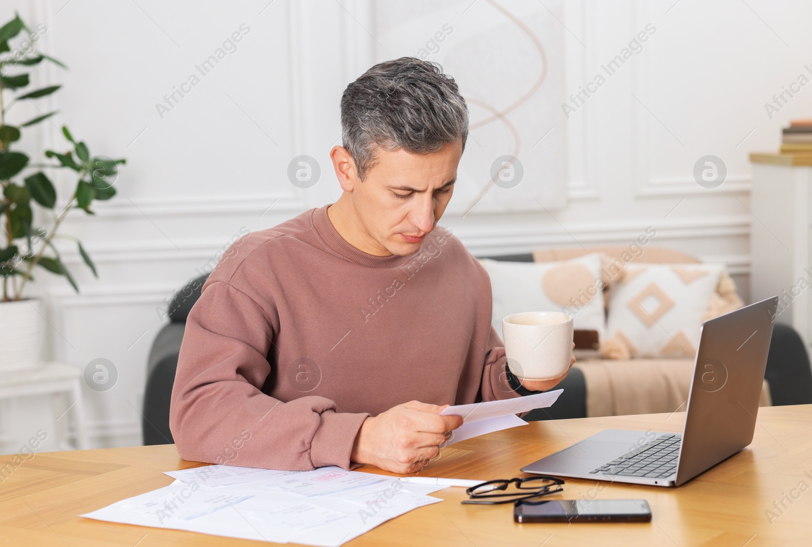 Photo of Man paying bills with laptop at wooden table indoors