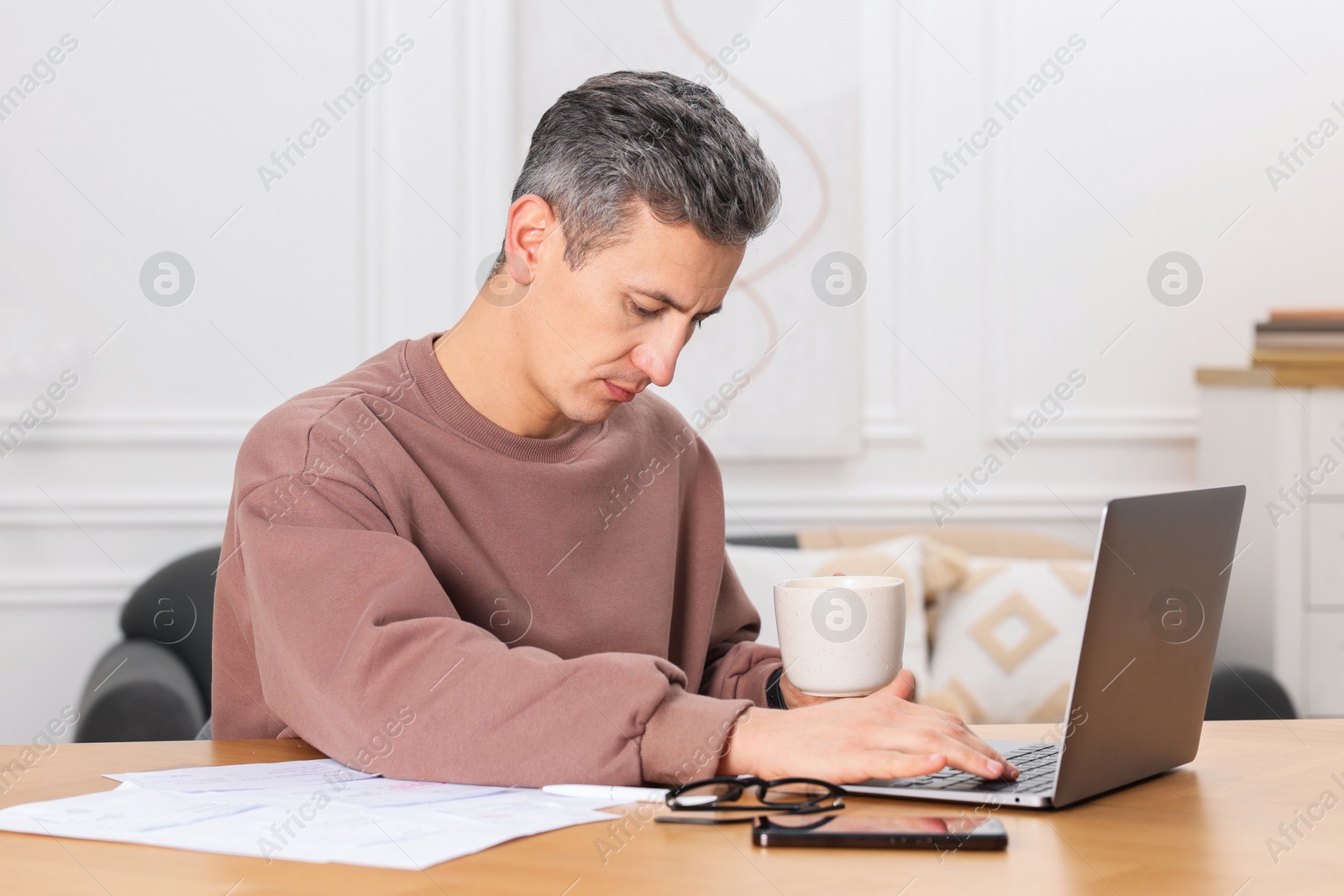 Photo of Man paying bills with laptop at wooden table indoors