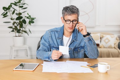 Photo of Paying bills. Man with different invoices talking on phone indoors