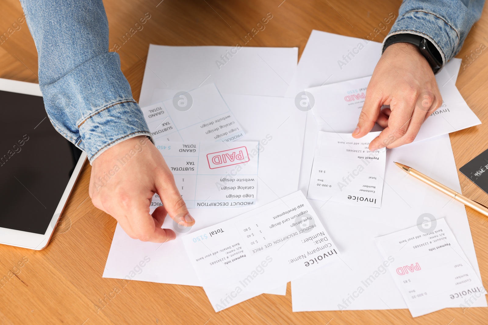 Photo of Paying bills. Man with different invoices and tablet at wooden table, closeup