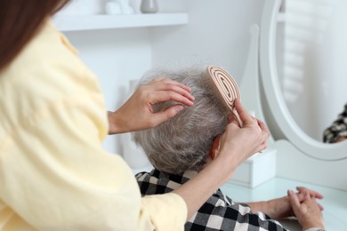 Photo of Woman brushing senior lady with brush indoors, closeup