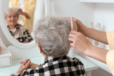 Photo of Woman brushing senior lady with brush indoors, closeup