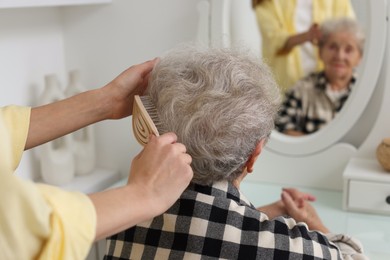 Photo of Woman brushing senior lady with brush indoors, closeup