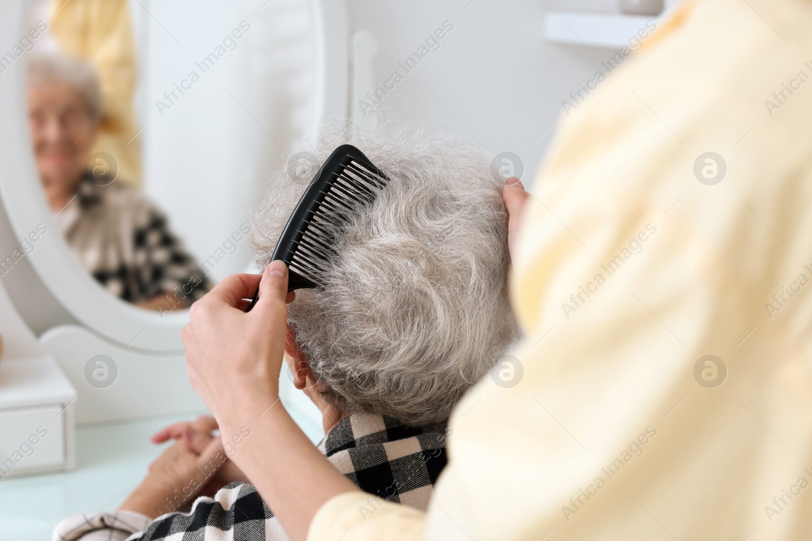 Photo of Woman brushing senior lady with comb indoors, closeup