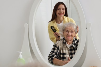 Photo of Woman brushing senior lady with comb indoors