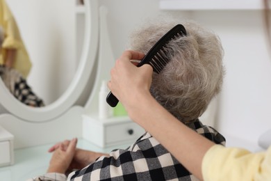 Photo of Woman brushing senior lady with comb indoors, closeup