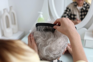 Photo of Woman brushing senior lady with comb indoors, closeup