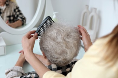 Photo of Woman brushing senior lady with comb indoors, closeup