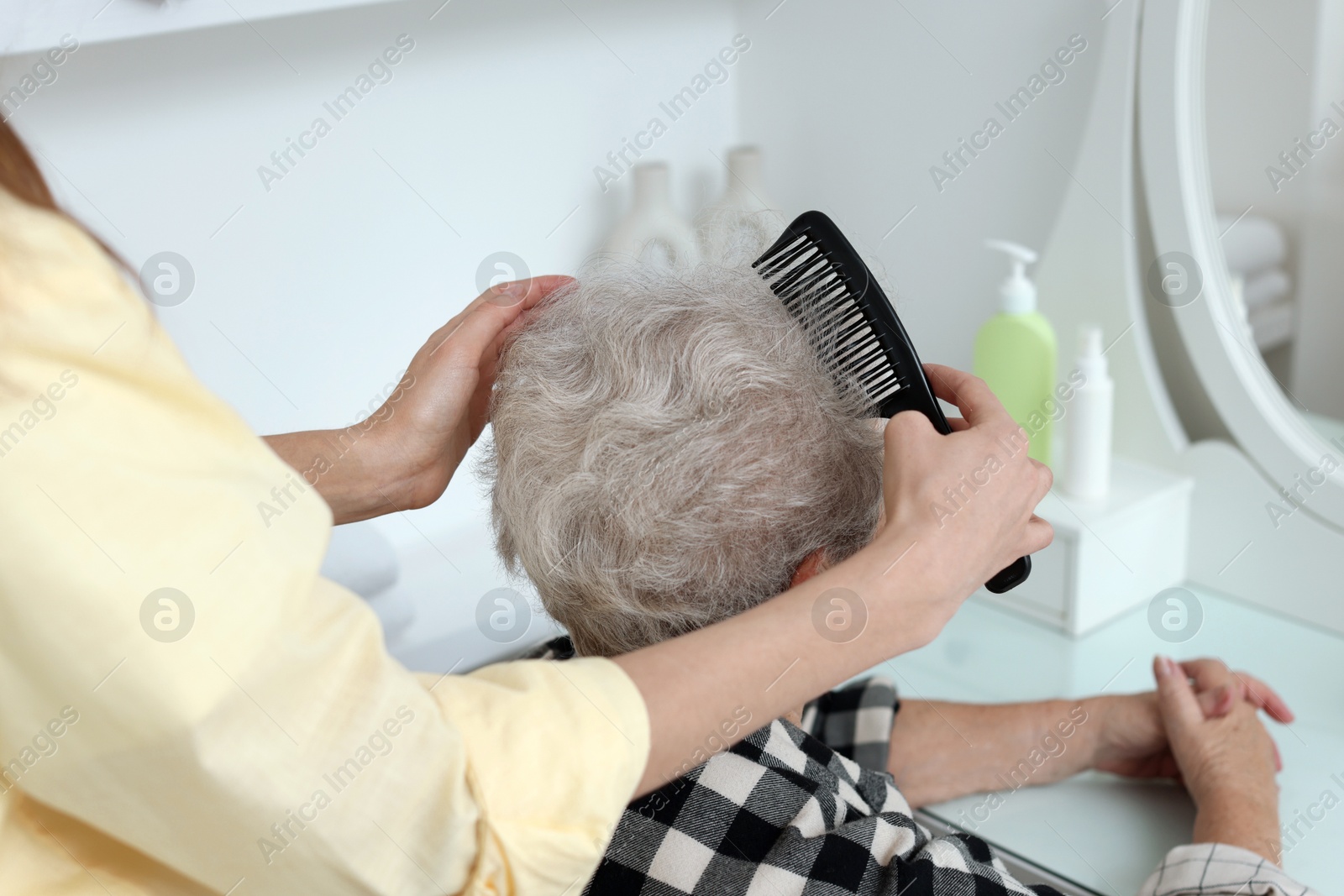 Photo of Woman brushing senior lady with comb indoors, closeup