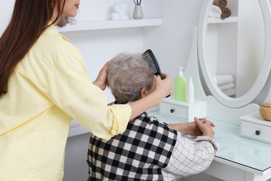 Photo of Woman brushing senior lady with comb indoors, closeup