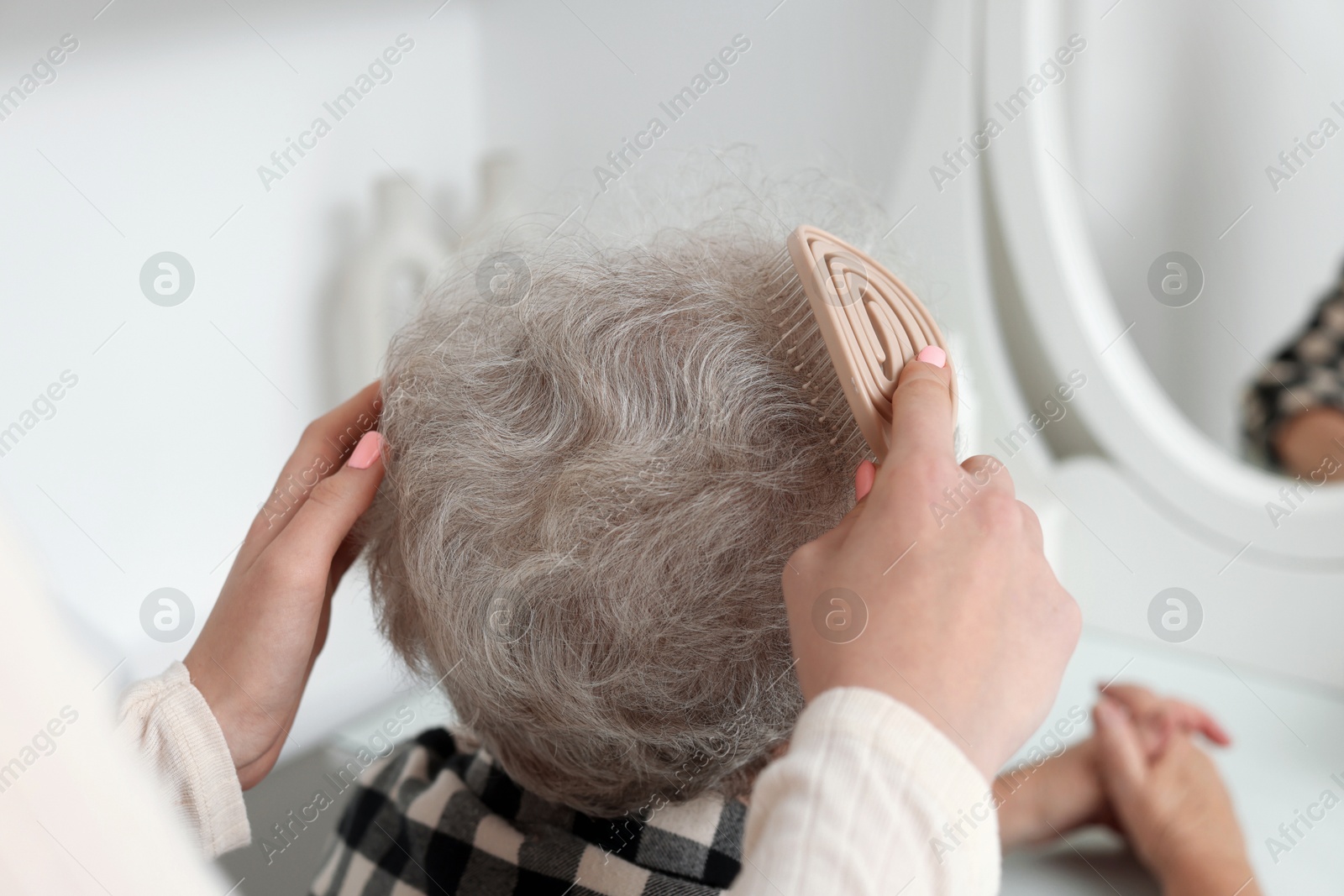 Photo of Granddaughter brushing her grandmother with brush at home, closeup