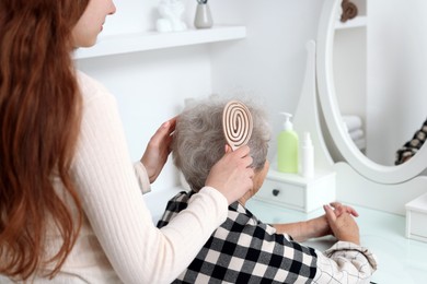 Photo of Granddaughter brushing her grandmother with brush at home, closeup