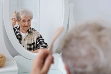 Photo of Senior woman brushing her hair with brush near mirror at home