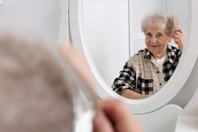 Photo of Senior woman brushing her hair with brush near mirror at home