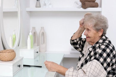 Photo of Senior woman brushing her hair with brush at dressing table indoors