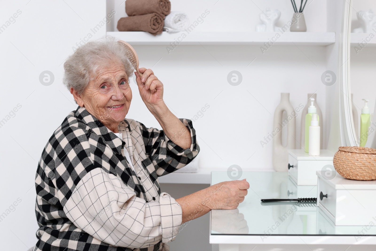 Photo of Senior woman brushing her hair with brush at dressing table indoors