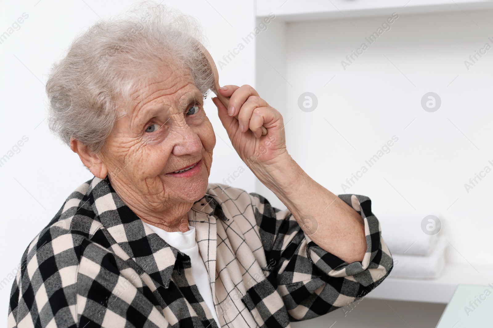 Photo of Senior woman brushing her hair with brush at home