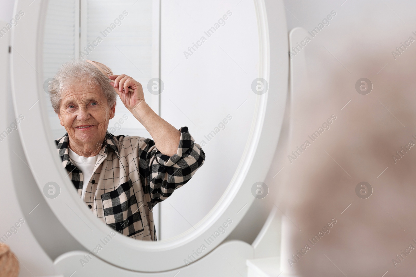 Photo of Senior woman brushing her hair with brush near mirror at home