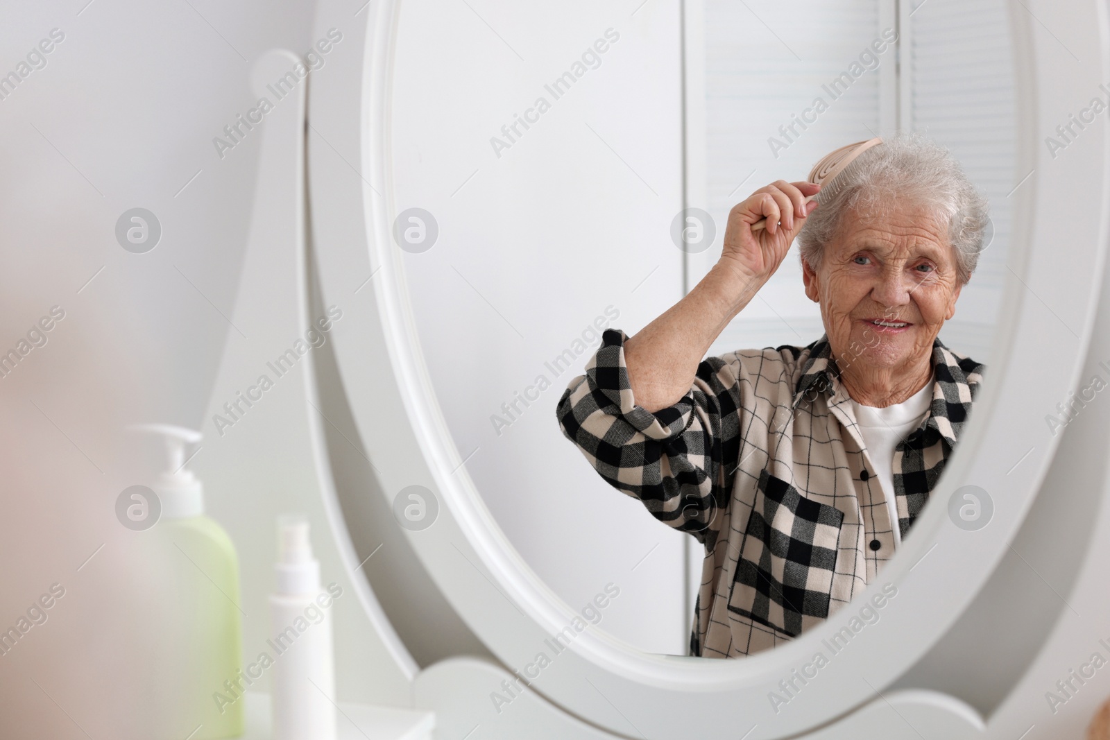 Photo of Senior woman brushing her hair with brush near mirror at home