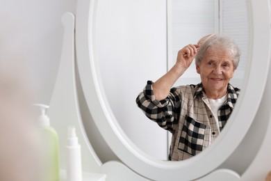 Photo of Senior woman brushing her hair with brush near mirror at home