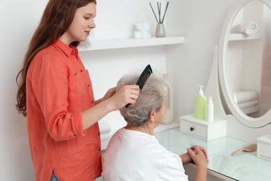 Photo of Granddaughter brushing her grandmother with comb at home